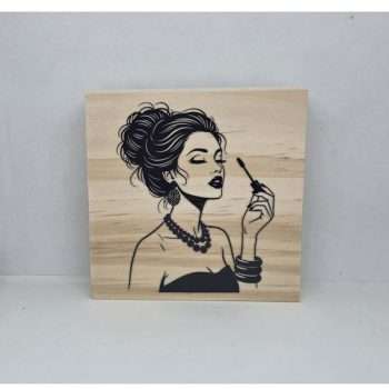 Glamorous Lady Shelf Sitter featuring a black illustration of an elegant woman applying makeup on a natural pine wood block displayed on a dressing table.